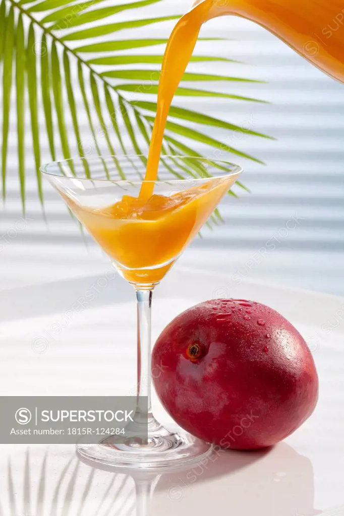 Mango juice being poured in martini glass besides mango