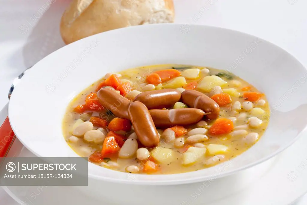 Bowl of bean soup with carrots, potatoes and mini sausages, close up