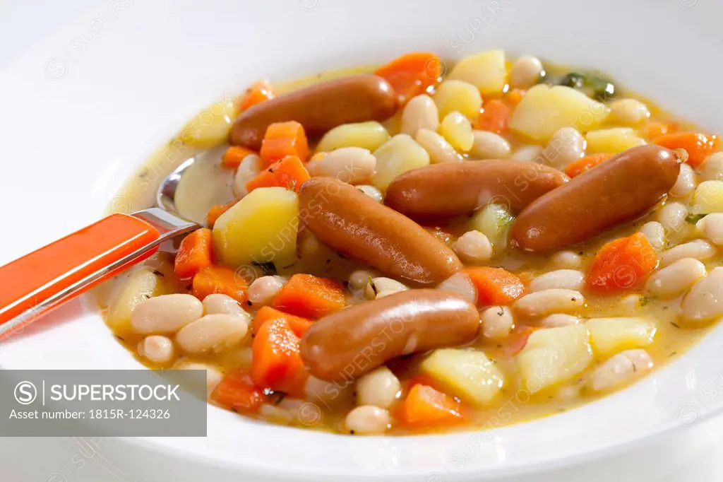 Bowl of bean soup with carrots, potatoes and mini sausages, close up