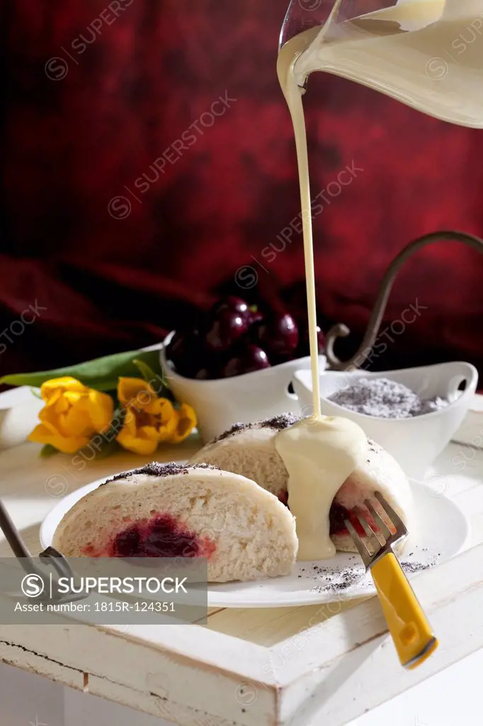 Pouring vanilla sauce on yeast dumplings with cherry filling and poppy seed