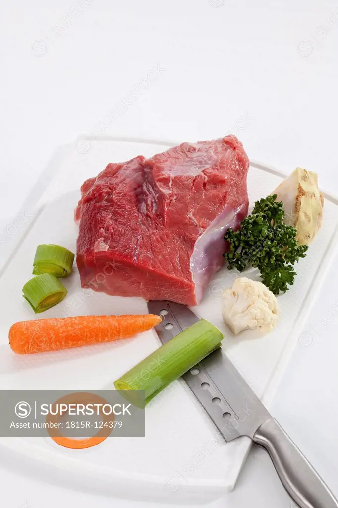 Raw piece of beef with vegetables on chopping board, close up