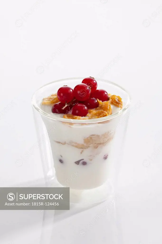 Glass of yogurt with muesli, cornflakes and red currants on white background, close up
