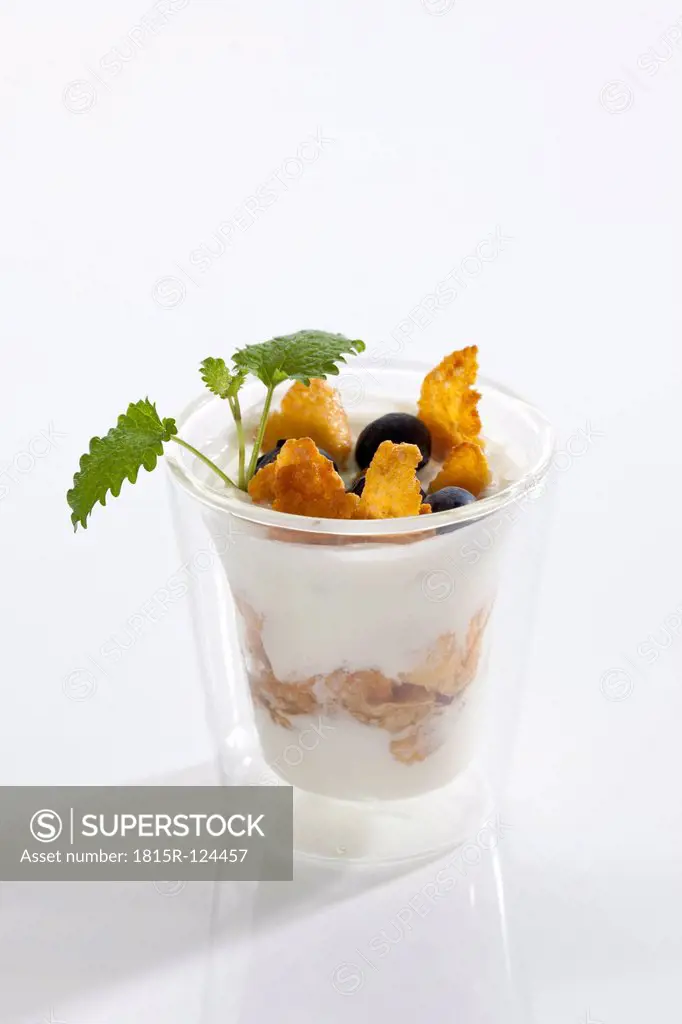 Glass of yogurt with muesli, blueberries and cornflakes on white background, close up