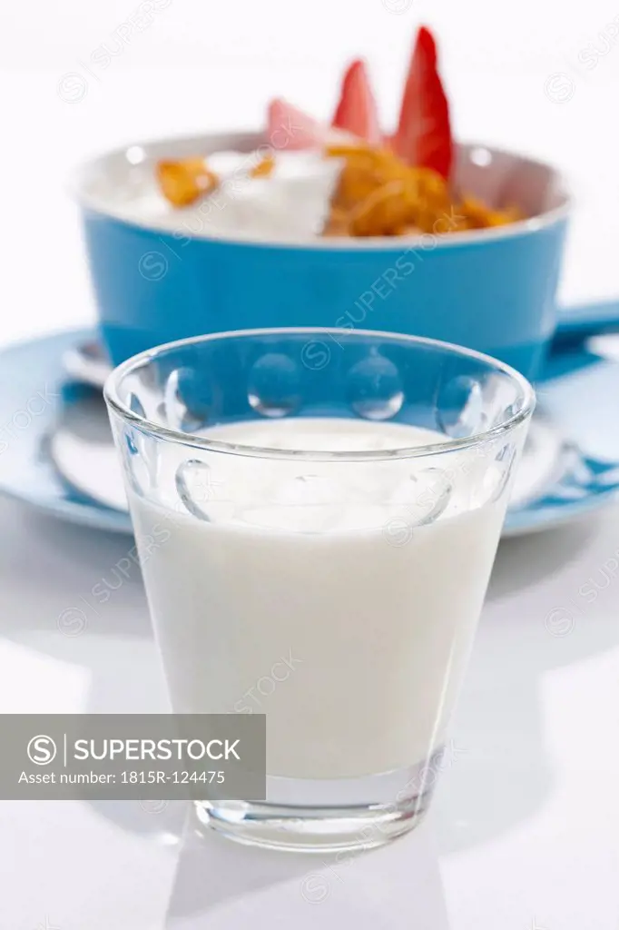 Glass of milk and bowl of cornflower with strawberries on white background