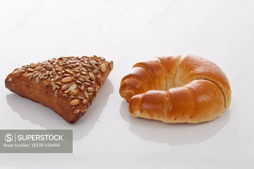 Croissant and grain bread on white background, close up