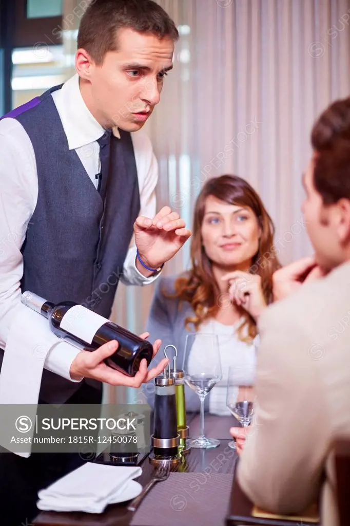 Waiter showing wine bottle to business associates at hotel restaurant