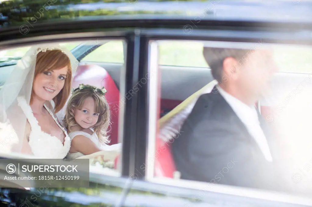 Bride sitting in car with little bridesmaid and driver before wedding