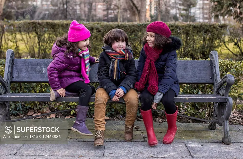 Three childrensitting on bench in a park on a winter day