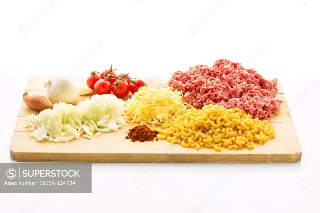 Minced meat, noodles, tomatoes, onions, garlic, cheese and spices on chopping board, close up