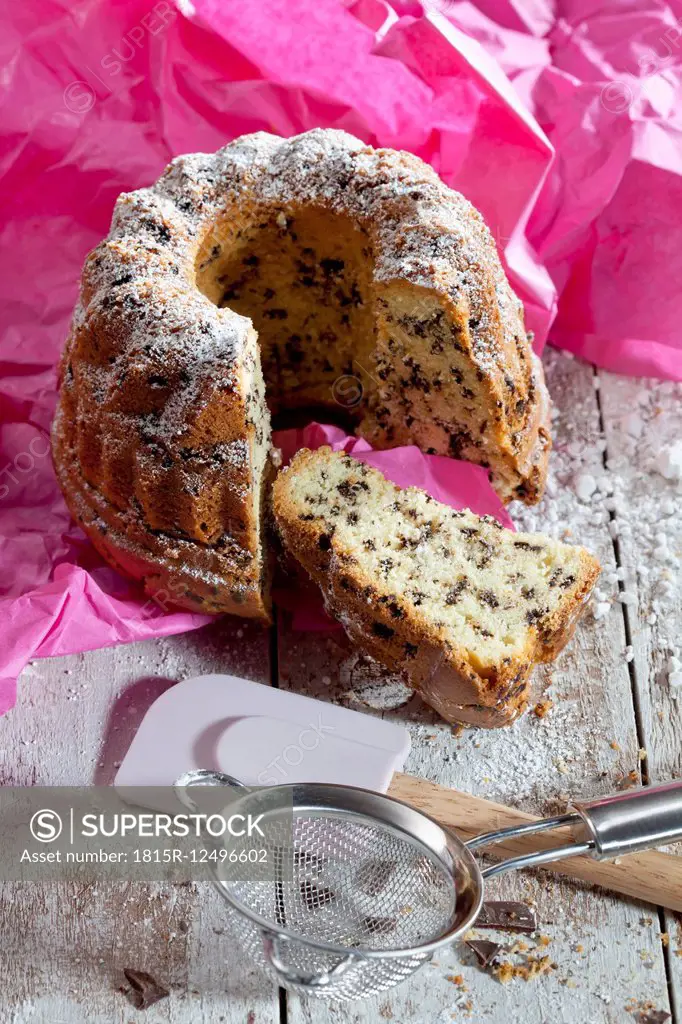 Sliced chocolate cake sprinkled with icing sugar, dough scraper and strainer