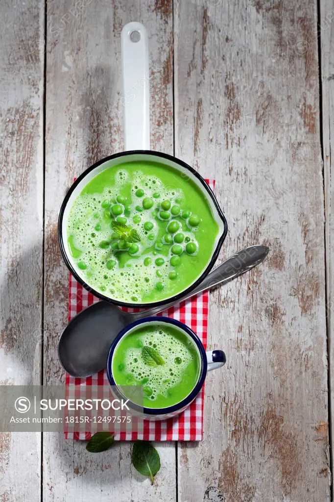 Saucepan and mug of pea soup, spoon and cloth on wood