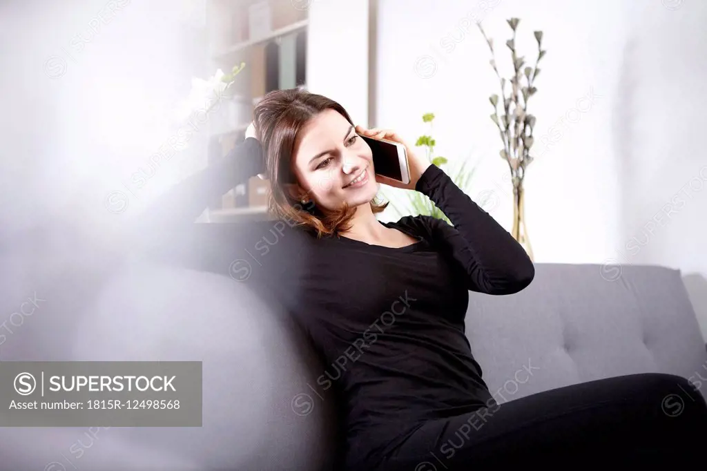 Smiling young woman sitting on couch telephonong with smartphone