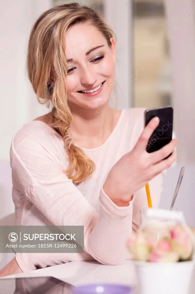 Portrait of smiling blond woman sitting in a coffee shop using smartphone