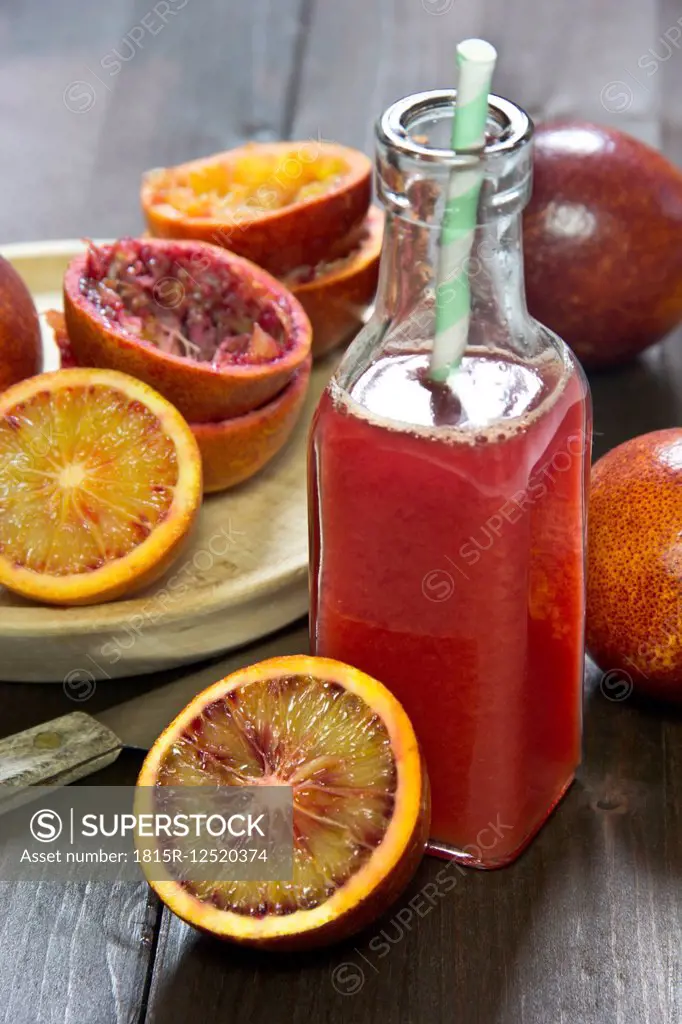 Glass bottle of blood orange juice, whole, sliced and squeezed blood oranges