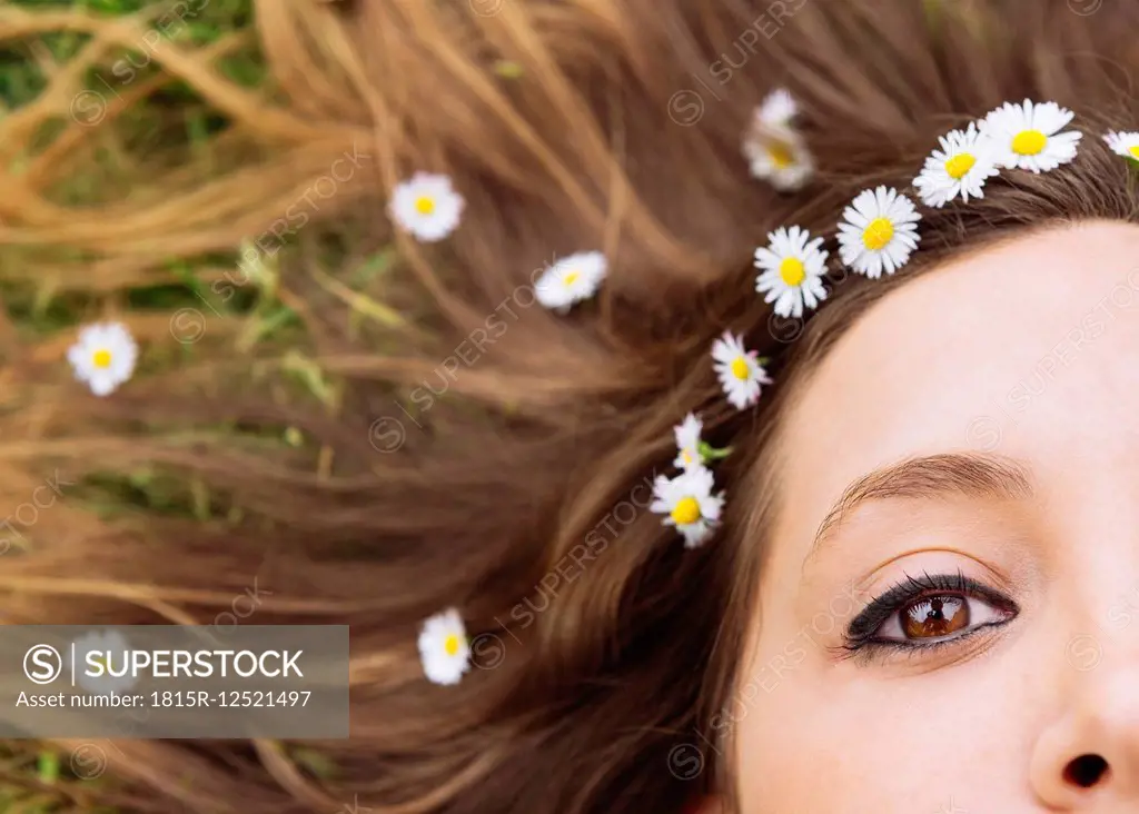 Woman lying on a meadow wearing daisies in her hair, close-up