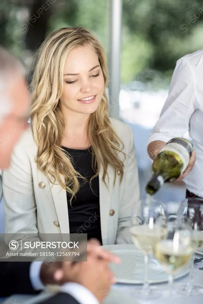 Waitress serving white wine to clients at table