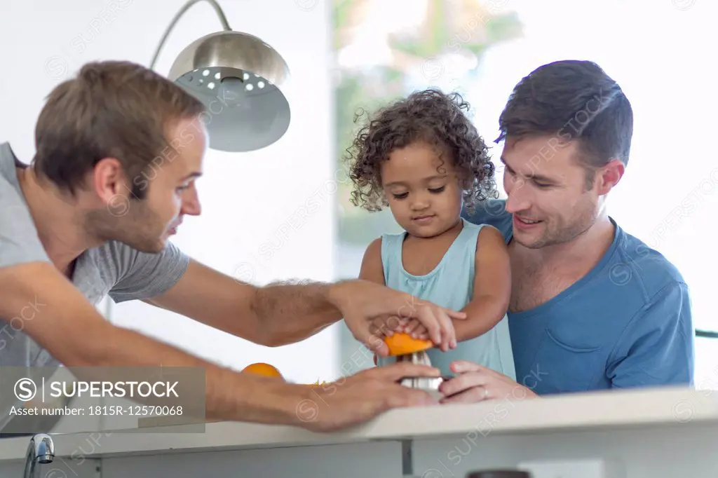 Gay couple with daughter making orange juice