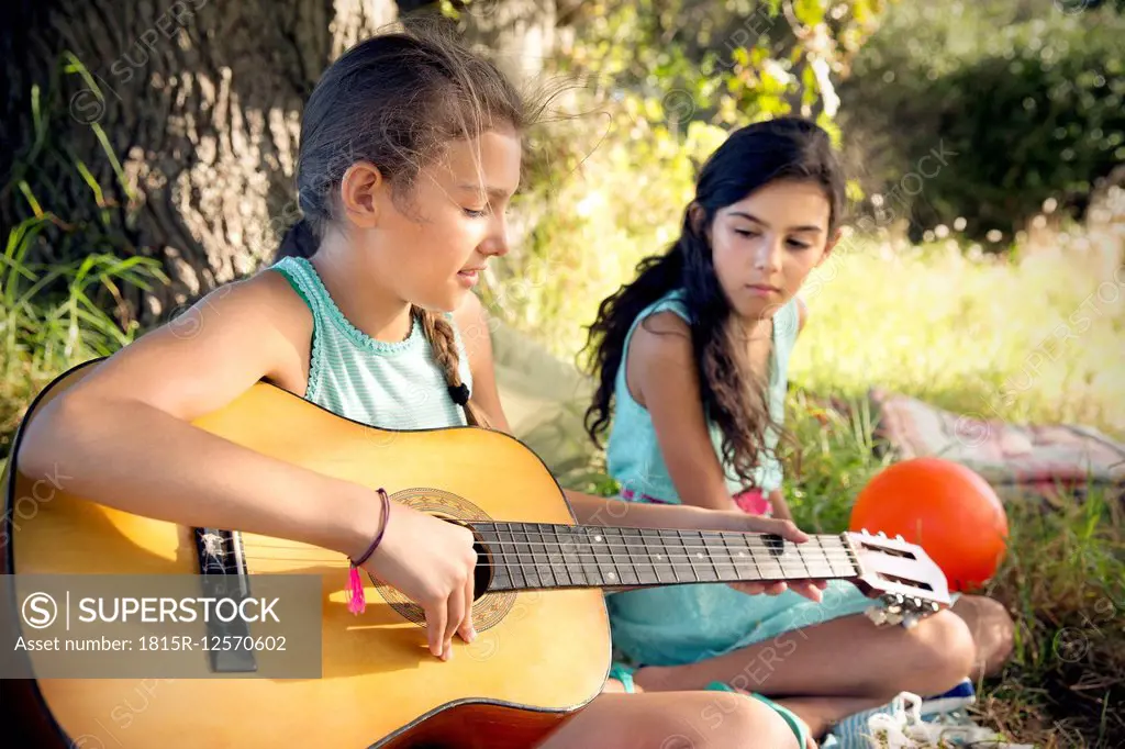 Girl in meadow playing guitar with sister watching