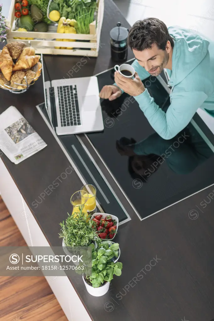 Man with cup of coffee and laptop in the kitchen