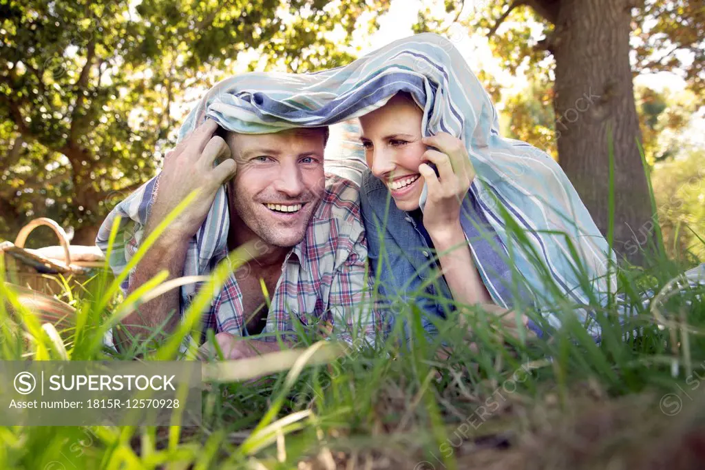 Happy couple lying on meadow under a blanket