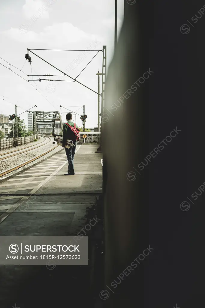 Young man with skateboard standing on railway platform