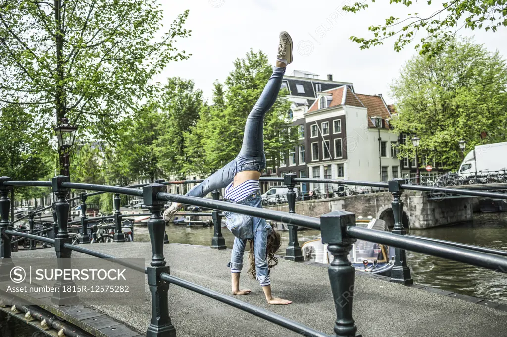 Netherlands, Amsterdam, female tourist doing handstand on footbridge