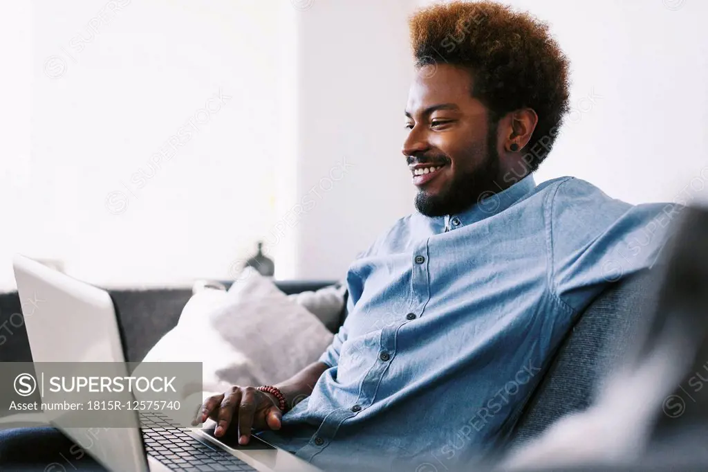 Young Afro American man sitting on couch, using laptop