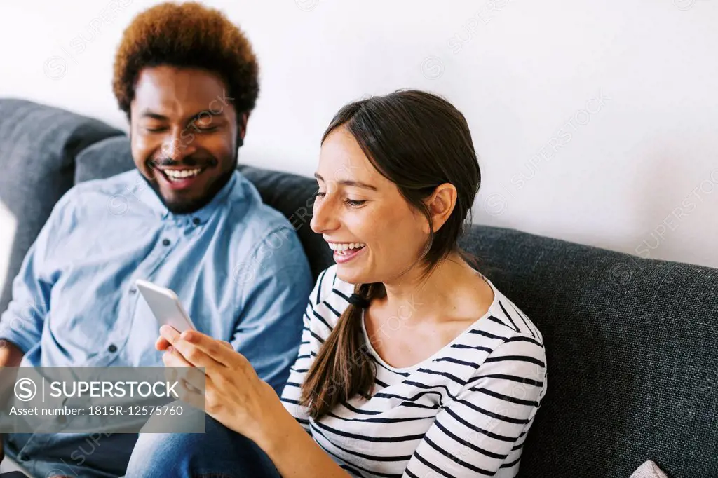 Young couple sitting on couch, using laptop and smart phone