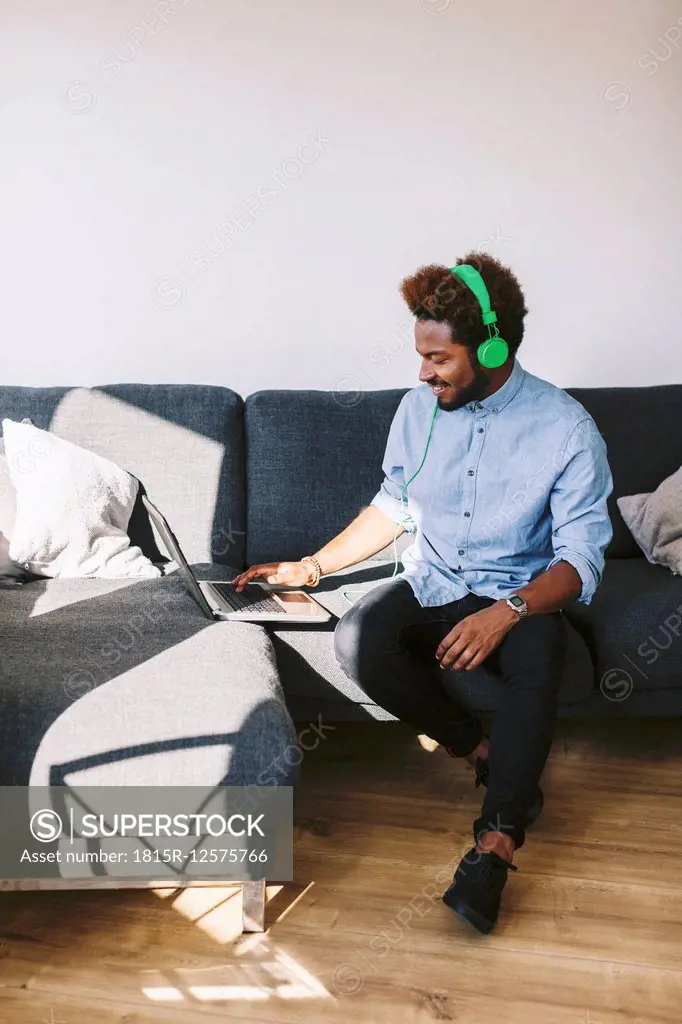 Young Afro American man sitting on couch, using laptop