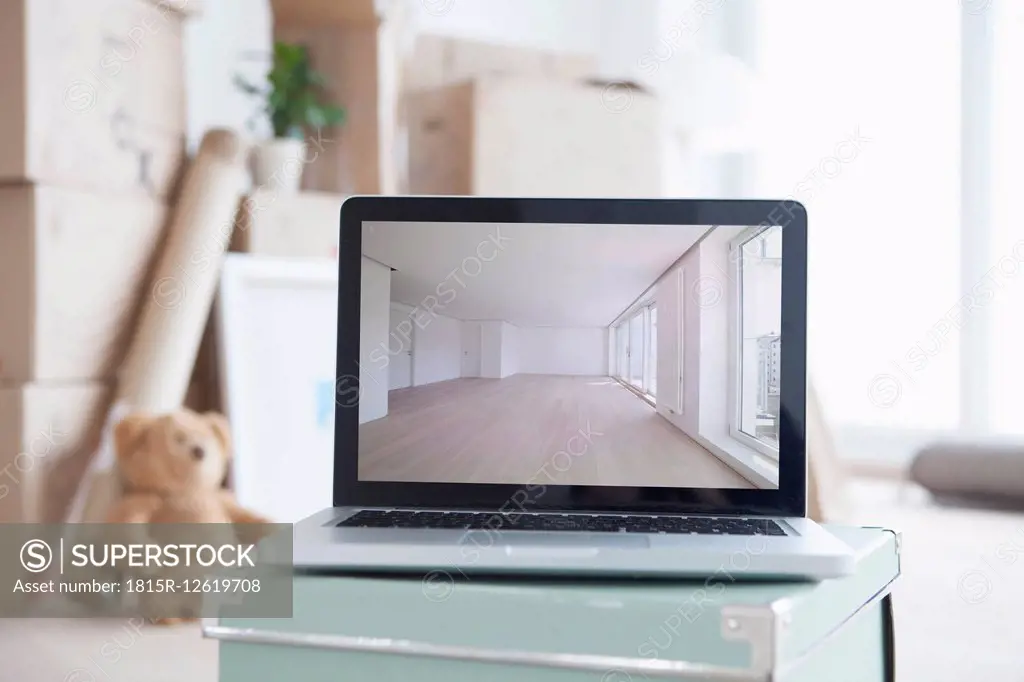 Laptop with picture of empty room in front of piled cardboard boxes