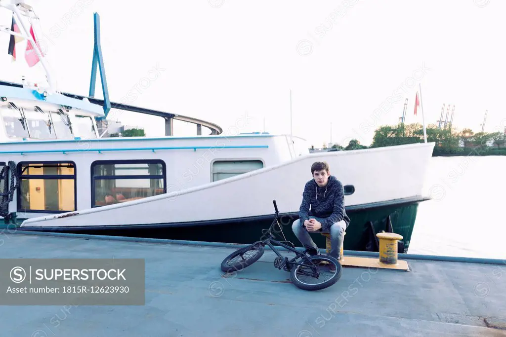 Germany, Hamburg, teenage boy with bmx bike sitting on a jetty