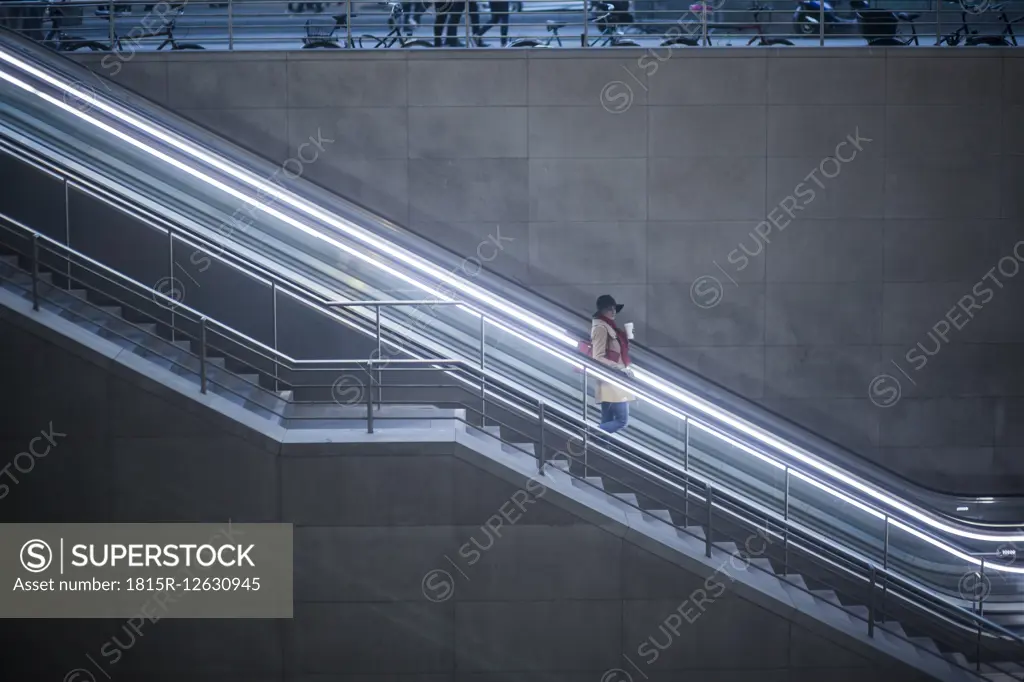 Young woman with coffee to go standing on escalator