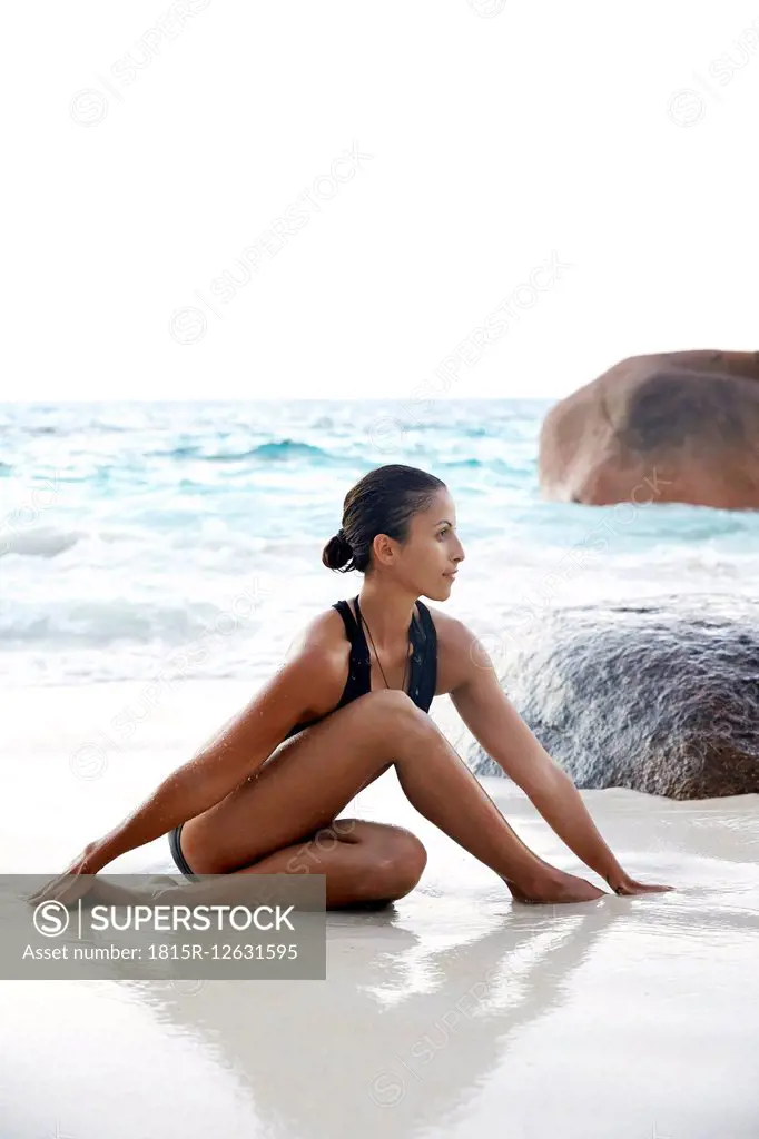 Seychelles, woman doing yoga exercise at seafront