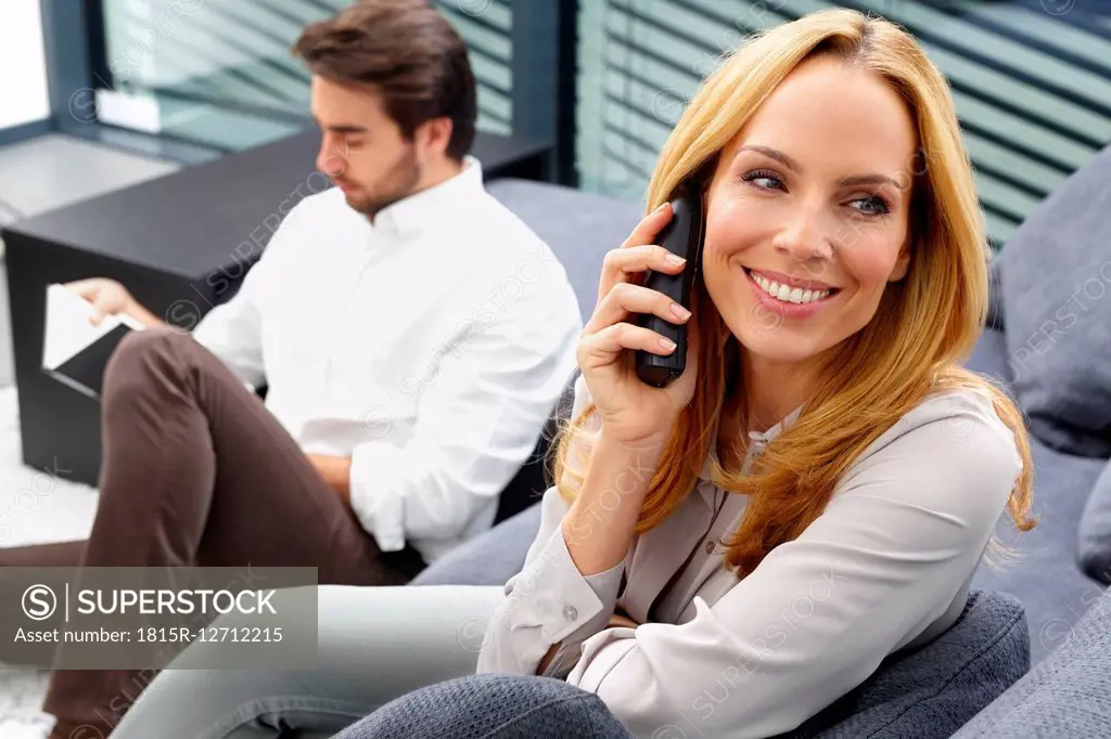Portrait of smiling woman talking on telephone while her husband sitting in the background