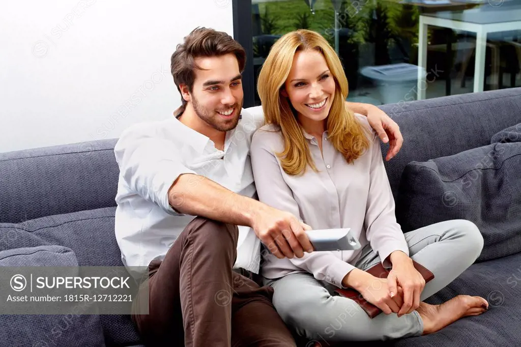 Happy couple sitting together on couch watching TV show