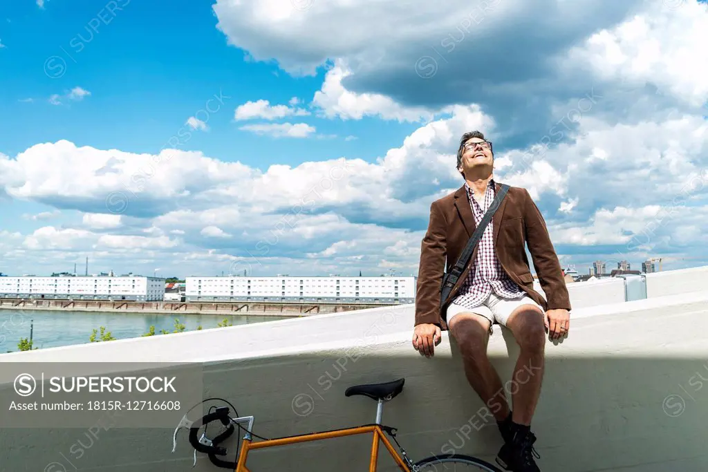 Mature man with bicycle sitting on wall enjoying weather