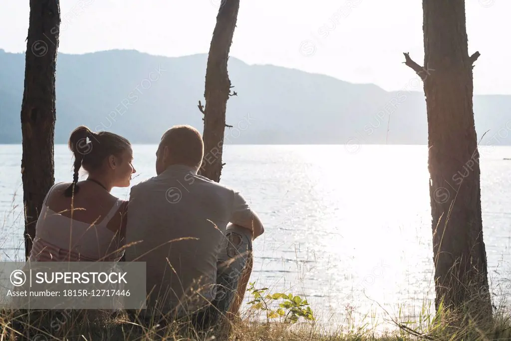 Bulgaria, Rhodope Mountains, couple sitting side by side at shore of Dospat Reservoir