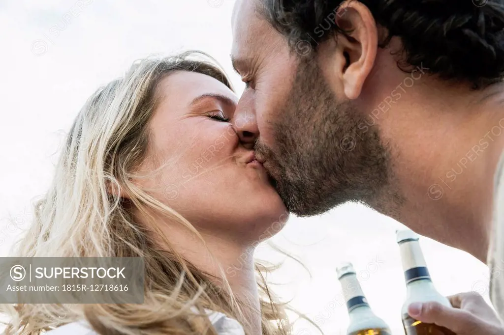 Couple with beer bottles kissing outdoors