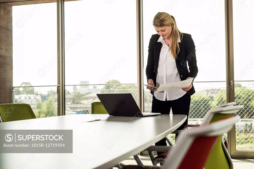 Young businesswoman in conference room with cell phone, laptop and documents