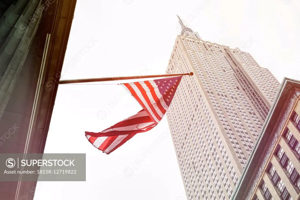 USA, New York City, Empire State Building with American flag in foreground