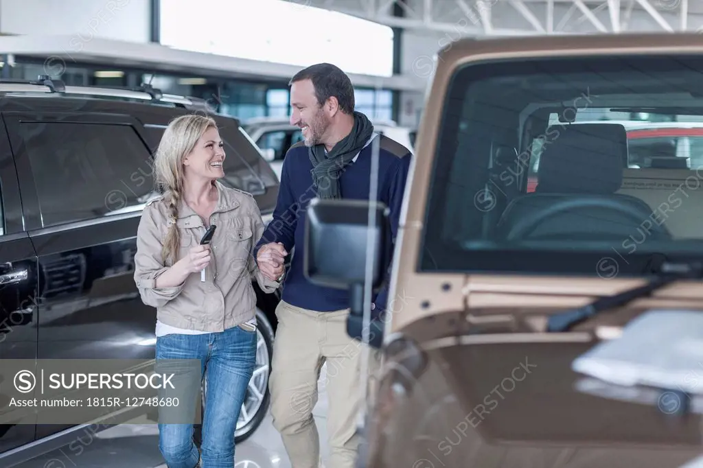 Happy couple at car dealership hand in hand at new car