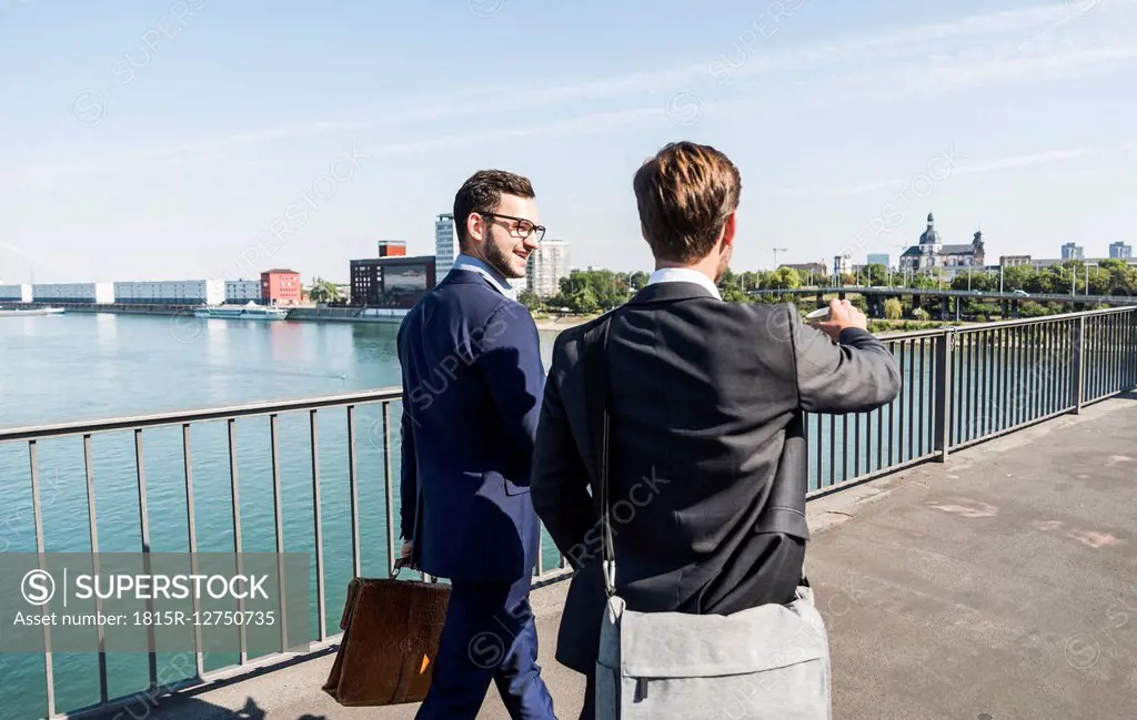 Two young business colleagues walking by river, discussing