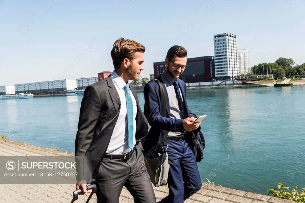 Two young businessmen on a business trip, walking by river