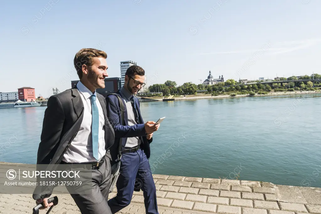 Two young businessmen on a business trip, walking by river