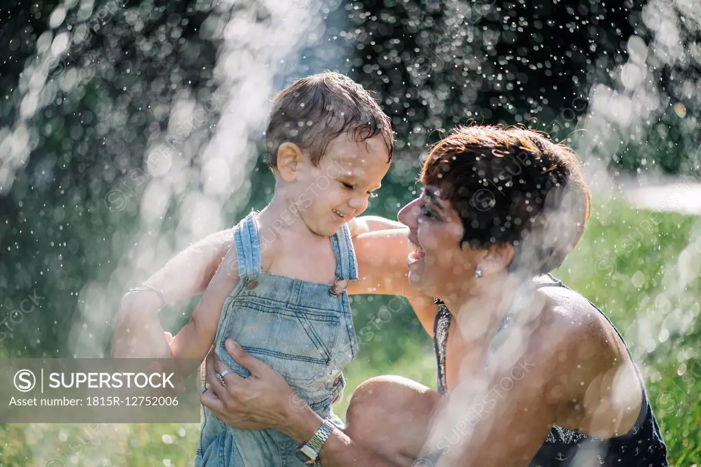 Happy little boy and his mother enjoying splashing water in the garden