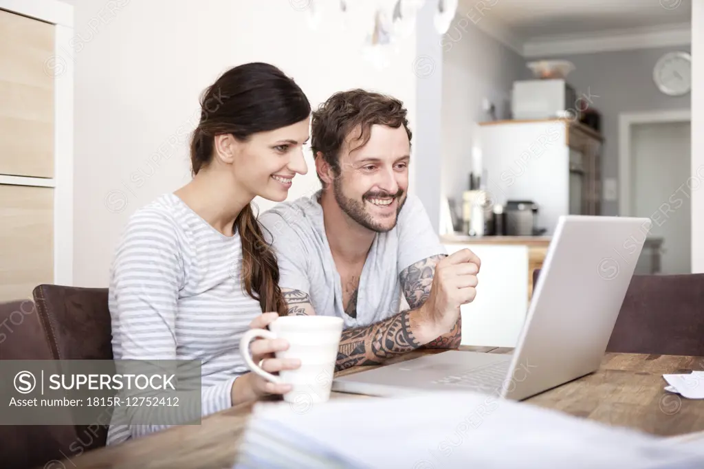 Smiling couple sitting at wooden table looking at laptop