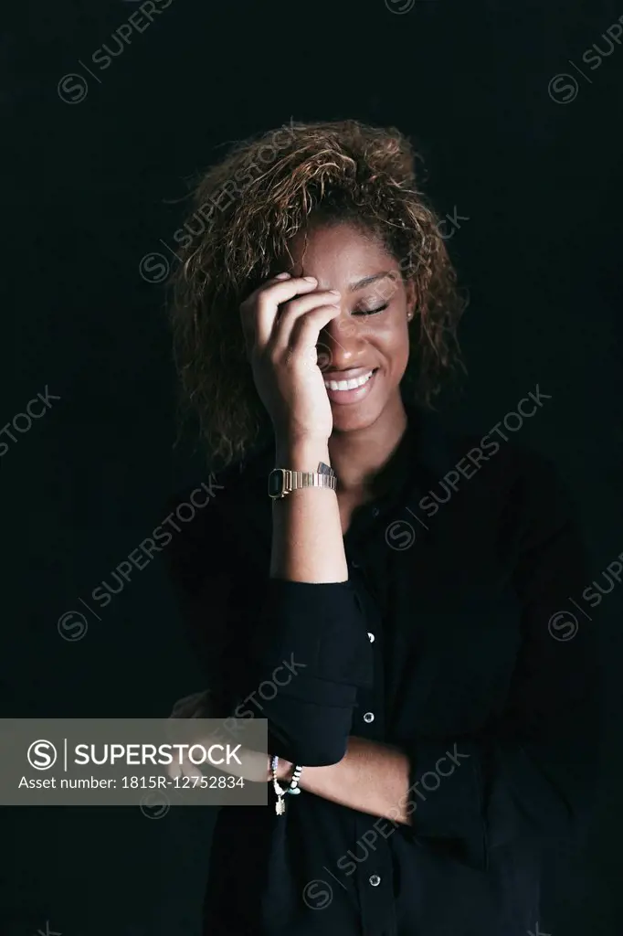Portrait of smiling woman with closed eyes and hand on her face in front of black background