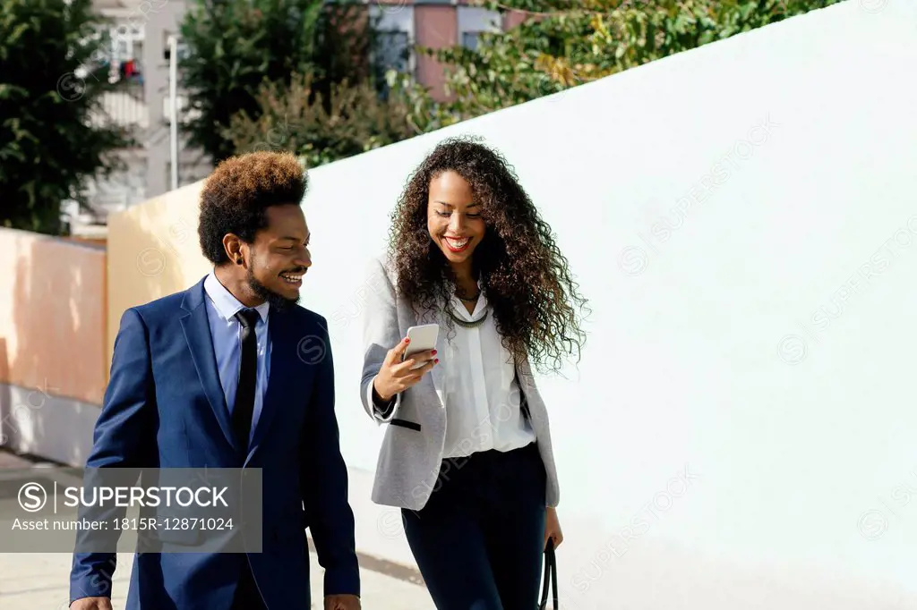 Portrait of two smiling young business people looking at smartphone
