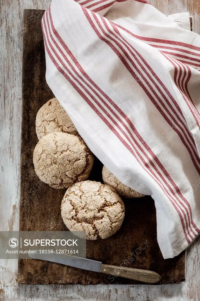 Homemade rye bread rolls on chopping board, kitchen towel