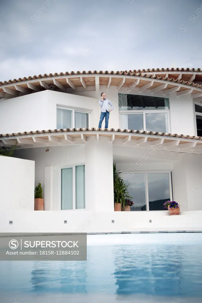 Spain, Mallorca, man standing on roof of his house telephoning